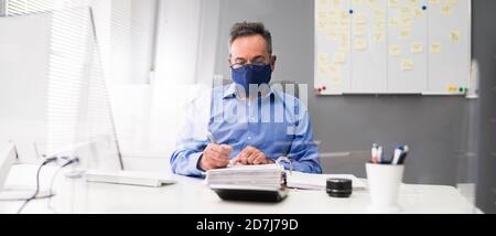 Ältester Geschäftsangestellte, Der Bei Computer Wearing Facial Mask Arbeitet Stockfoto