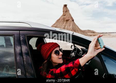 Spanien, Navarra, Frau Touristen lehnt aus dem Auto Fenster nehmen Smartphone-Fotos von Bardenas Reales Stockfoto