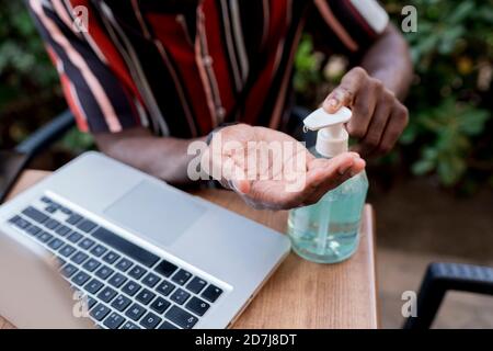 Junger Mann mit Handdesinfektionsmittel, während er mit einem Laptop sitzt Café Stockfoto