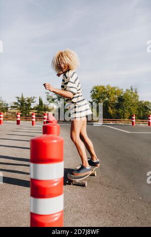 Blonde weibliche Skateboarderin geht durch Hindernisparcours auf Straße gegen Himmel Stockfoto