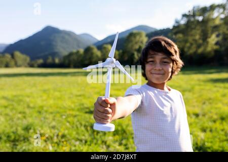 Lächelnder Junge hält Windturbine Spielzeug, während er auf der Wiese steht Stockfoto