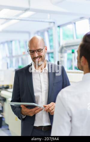 Lächelnder Geschäftsmann, der beim Gespräch mit jungen Menschen auf ein digitales Tablet schaut Männlicher Kollege im Werk Stockfoto