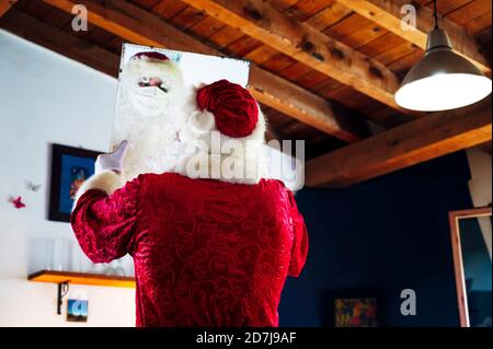 Mann trägt Weihnachtsmann Kostüm Blick in Spiegel während des Stehens Zu Hause Stockfoto