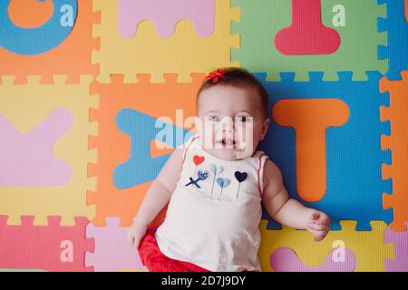 Nettes Baby Mädchen auf bunten alphabetischen Puzzle Playmat entspannen Zu Hause Stockfoto