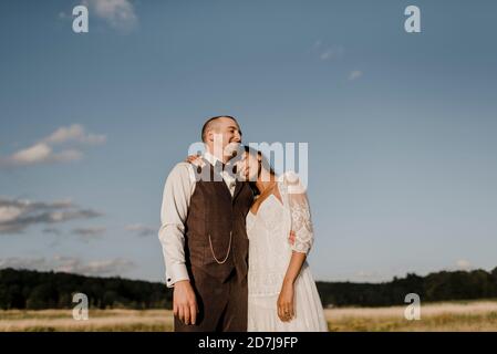 Die Braut lehnt sich auf die Schulter des Bräutigams, während sie auf dem Feld steht Stockfoto