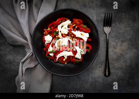 Schüssel vegetarischer Salat mit roten Paprika, Mozzarella, gerösteten Pinienkernen, Petersilie und Schnittlauch Stockfoto