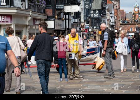 Mädchen, das eine Spende an RNLI auf einer belebten Eastgate Street in Chester, England macht Stockfoto