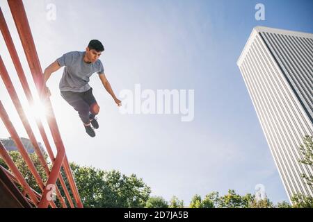 Der junge Mann springt über das Geländer und parkour gegen den klaren Himmel In der Stadt Stockfoto