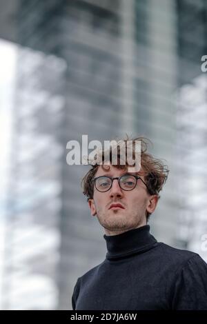 Nahaufnahme eines ernsthaften jungen Mannes, der eine Brille gegen das Gebäude trägt Stockfoto