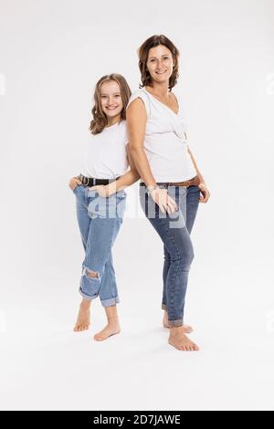 Lächelnde Mutter und Tochter mit den Händen in den Taschen während posiert Stehen vor weißem Hintergrund Stockfoto