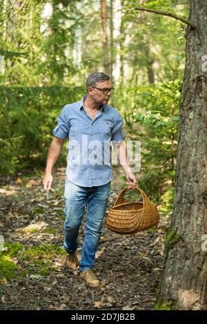 Reifer Mann zu Fuß mit Korb auf der Suche nach Pilz im Wald Stockfoto