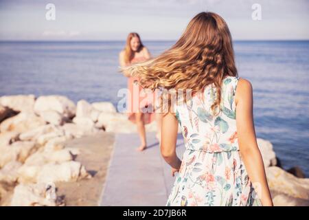 Lächelnde Mädchen, die an sonnigen Tagen auf dem Bürgersteig gegen das Meer spielen Stockfoto