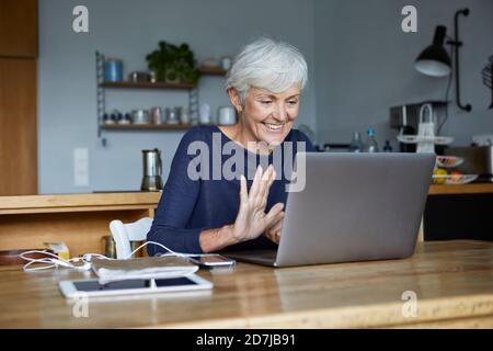 Aktive ältere Frau, die während eines Videoanrufs hohe fünf macht Mit Laptop zu Hause Stockfoto