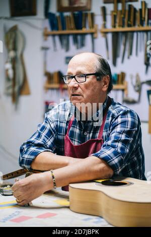 Nachdenklicher Mann, der in der Werkstatt am Tisch steht Stockfoto