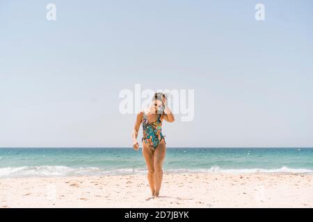 Frau mit Body und Sonnenbrille beim Spaziergang am Strand von Valdevaqueros, Tarifa, Spanien Stockfoto