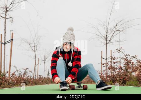 Junge Frau binden Schnürsenkel, während auf Skateboard sitzen Stockfoto