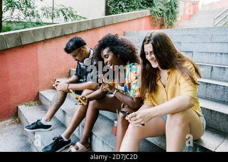 Junge Frau nimmt Selfie, während Freunde SMS auf smart Telefon sitzt auf Stufen Stockfoto