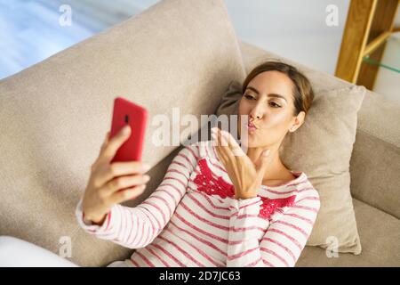 Frau, die auf einem Videoanruf küsst, während sie auf dem Sofa liegt Zu Hause Stockfoto