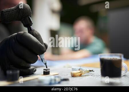 Hand des männlichen Künstlers Tauchen Tattoo Maschine in Tinte auf Tabelle Stockfoto