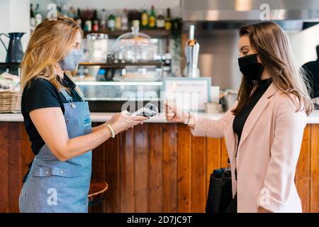 Geschäftsfrau in Gesichtsmaske, die im Café mit Kreditkarte bezahlt Während der Coronavirus-Krise Stockfoto