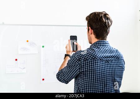 Junger Mann, der am Whiteboard ein Foto von der Papiernadel gemacht hat Büro Stockfoto