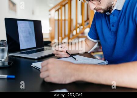 Mittelteil des jungen Mannes, der am Tisch Mathematik macht Stockfoto