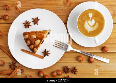 Stück hausgemachter Kuchen mit Mandeln und weißer Tasse Kaffee Cappuccino auf einem Holztisch. Draufsicht. Stockfoto