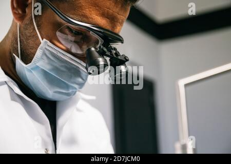 Männlicher Zahnarzt trägt Maske und chirurgische Lupen während der Arbeit in Klinik Stockfoto