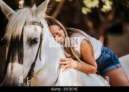 Schöne junge Frau, die sich auf ein weißes Pferd stützt Stockfoto