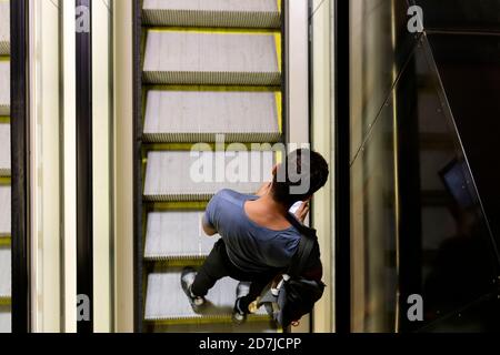 Mann, der Smartphone benutzt, während er auf der Rolltreppe bei beleuchtet steht U-Bahn Stockfoto