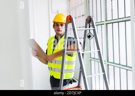 Architekt trägt Arbeitshelm und Jacke stehen an der Leiter in Büro im Bau Stockfoto