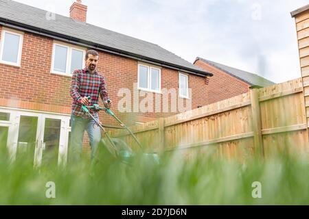 Mann mäht Rasen mit Rasenmäher im Hinterhof Stockfoto