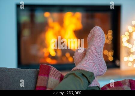 Beine der jungen Frau in Socken entspannend gegen Kamin an Zu Hause Stockfoto