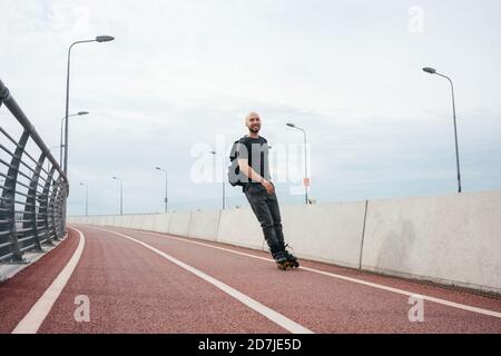 Junger Mann Inline-Skating auf Brücke gegen bewölkten Himmel in Stadt Stockfoto