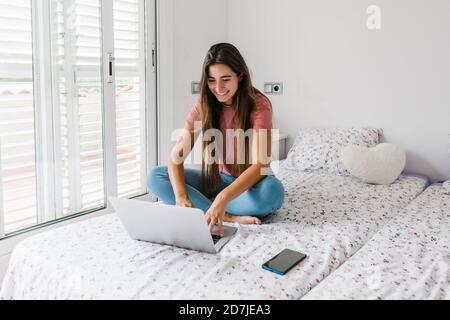 Junge Frau, die auf dem Laptop studiert, während sie im Schlafzimmer sitzt Zu Hause Stockfoto