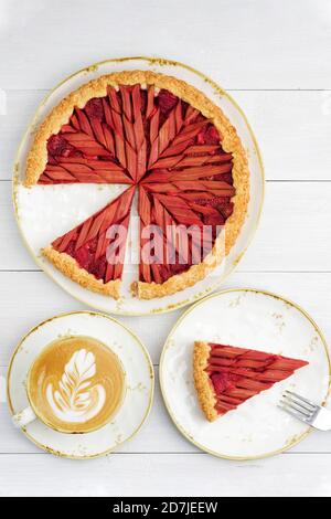 Hausgemachter Rhabarber- und Erdbeerkuchen und Tasse Kaffee auf weißem Holztisch. Draufsicht. Stockfoto