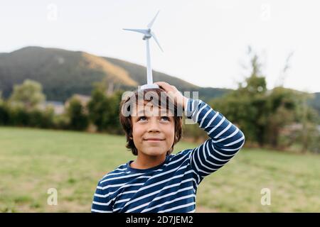 Lächelnder Junge hält Windturbinenspielzeug auf dem Kopf, während er steht Im Hinterhof Stockfoto