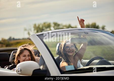 Fröhliche Freundinnen genießen Roadtrip im Cabrio gegen Himmel Bei Sonnenuntergang Stockfoto