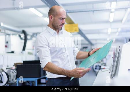 Selbstbewusster reifer männlicher Ingenieur, der große Leiterplatte bei Beleuchtung analysiert Werk Stockfoto