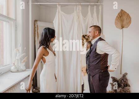 Lächelndes Paar, das sich ansieht, während es bei der Hochzeit steht Kleiderladen Stockfoto