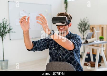 Lächelnder Architekt mit Visual Reality-Simulator, während er auf einem Stuhl sitzt Im Büro Stockfoto