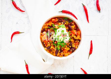 Schüssel mit vegetarischem Eintopf mit roten Linsen, Chilischoten, Sellerie, Nierenbohnen, Tomaten, Karotten und saurer Sahne Stockfoto