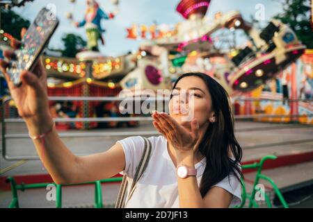 Junge Frau weht Kuss während Selfie im Vergnügungspark Stockfoto