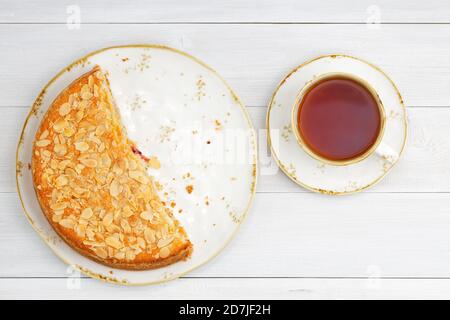 Die Hälfte der hausgemachten Stachelbeerpastete garniert mit Mandelblüten und einer Tasse Tee auf dem weißen Holztisch. Draufsicht. Stockfoto