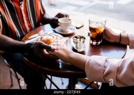 Romantisches junges Paar, das die Hände hält, während es im Kaffee trinkt Kaufen Stockfoto