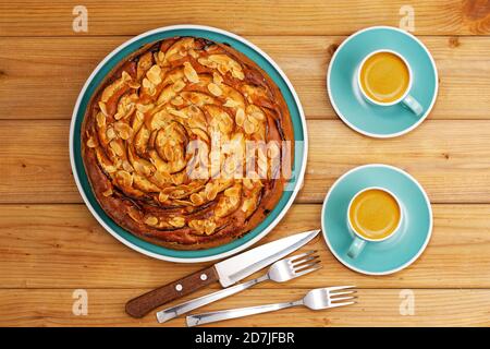 Hausgemachter Kuchen mit Äpfeln und Pflaumen mit Mandelblüten und zwei Tassen Kaffee Espresso auf Holztisch. Draufsicht. Stockfoto