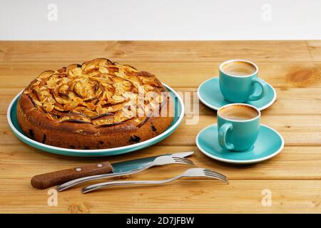 Hausgemachter Kuchen mit Äpfeln und Pflaumen mit Mandelblüten und zwei Tassen Kaffee Espresso auf Holztisch. Stockfoto