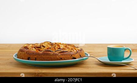 Hausgemachter Kuchen mit Äpfeln und Pflaumen mit Mandelblüten und Tasse Kaffee Espresso auf Holztisch. Stockfoto