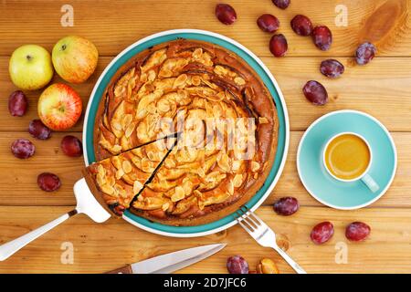 Hausgemachter Kuchen mit Äpfeln und Pflaumen mit Mandelblüten und Tasse Kaffee Espresso auf Holztisch. Draufsicht. Stockfoto