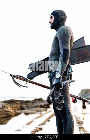 Mann trägt Neoprenanzug hält Scuba Maske und Harpune während des Stehens Am Strand gegen klaren Himmel Stockfoto